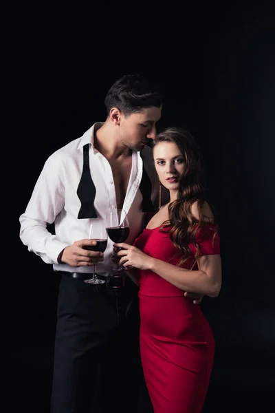 Atractiva pareja sosteniendo copas de vino tinto aisladas en negro - foto de stock