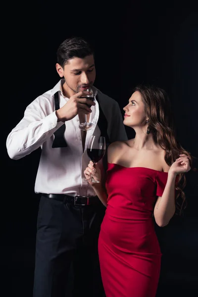 Beau couple souriant boire vin rouge isolé sur noir — Photo de stock