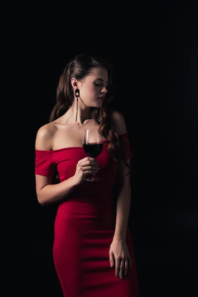 Mulher atraente em vestido vermelho segurando copo de vinho tinto isolado em preto — Fotografia de Stock