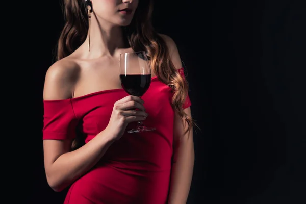 Vista parcial de la mujer en vestido rojo sosteniendo copa de vino tinto aislado en negro - foto de stock