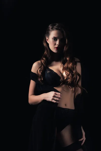 Mujer seductora mirando a la cámara y posando en lencería aislada sobre negro - foto de stock