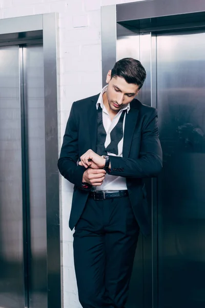 Man in black suit putting on watch near elevators — Stock Photo