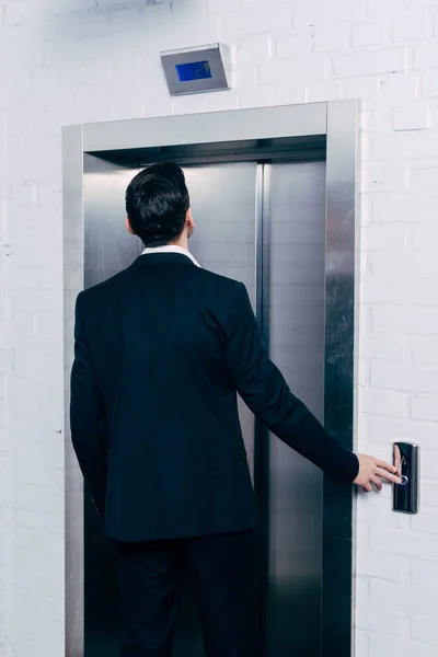 Back view of man in black suit pressing elevator button — Stock Photo