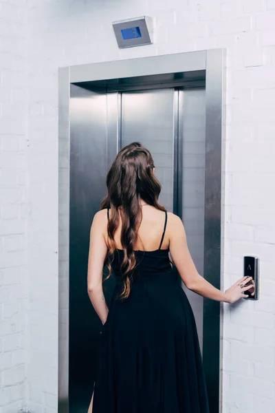 Vista trasera de la mujer en vestido negro presionando el botón del ascensor - foto de stock