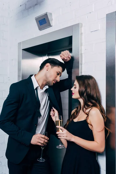 Couple romantique tenant des verres de champagne, parler et attendre l'ascenseur — Photo de stock