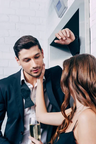 Femme tenant verre de champagne et toucher le visage de l'homme en attendant l'ascenseur — Photo de stock