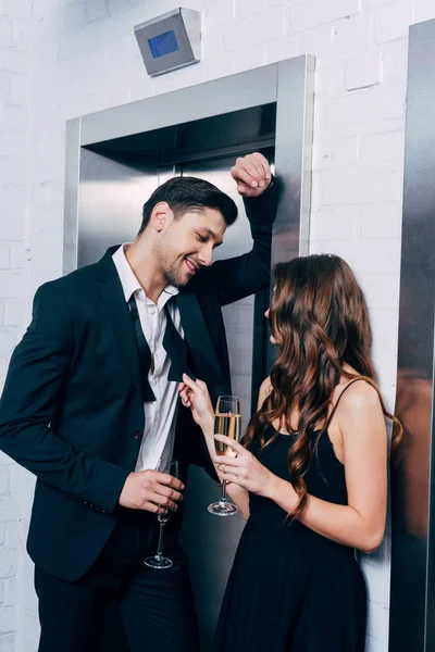 Couple in formal wear holding champagne glasses, talking and waiting for elevator — Stock Photo