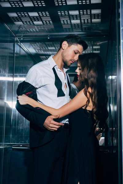 Mujer en vestido negro apasionadamente desvestirse hombre guapo en ascensor - foto de stock