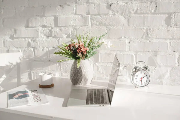 Laptop near business newspaper, cup and vase with flowers in kitchen — Stock Photo