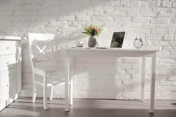 Ноутбук в белой кухне возле чашки и вазы с цветами на кухне — стоковое фото