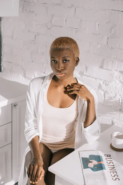 Selbstbewusste afrikanisch-amerikanische Frau sitzt in weißer Küche — Stockfoto