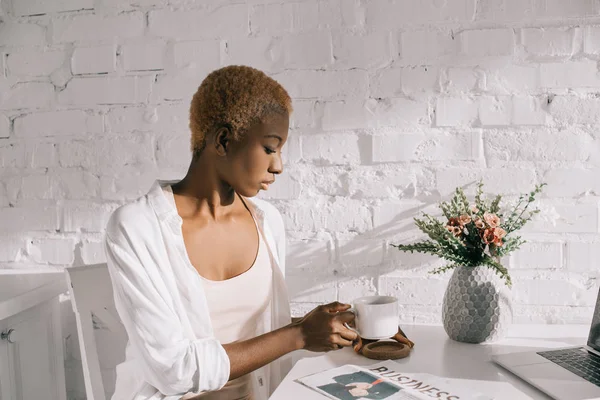 Bela mulher africana americana segurando copo na cozinha branca — Fotografia de Stock