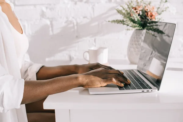 Vue recadrée de femme afro-américaine en utilisant un ordinateur portable dans la cuisine blanche — Photo de stock