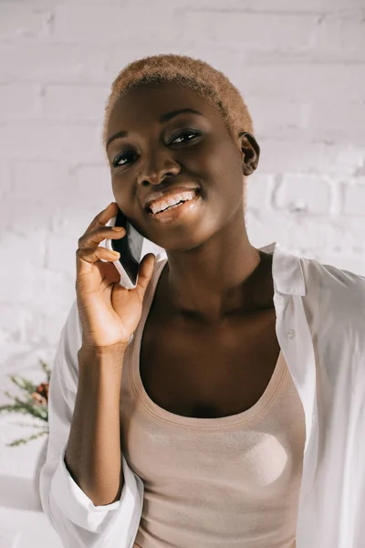 Mujer afroamericana con el pelo corto sonriendo y hablando en el teléfono inteligente - foto de stock