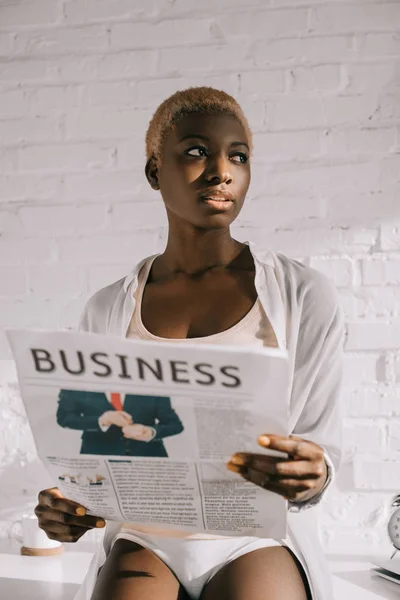 Mujer afroamericana reflexiva con pelo corto lectura periódico de negocios - foto de stock