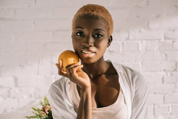 Donna afroamericana con i capelli corti in possesso arancione in cucina bianca — Foto stock