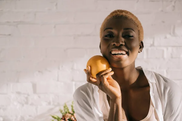 Cheerful african american woman with short hair holding orange — Stock Photo