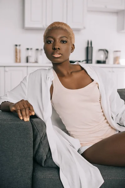 Atractiva mujer afroamericana con pelo corto sentado en el sofá en la sala de estar - foto de stock