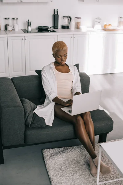 Focused african american woman typing on laptop in living room — Stock Photo