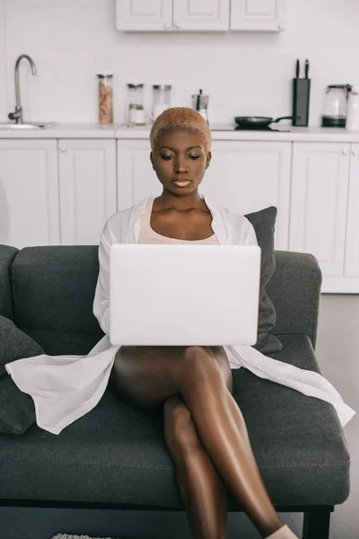 Hermosa mujer afroamericana escribiendo en el ordenador portátil en la sala de estar - foto de stock