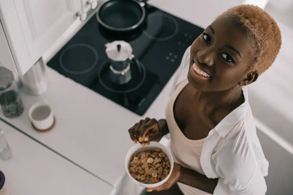 Blick von oben auf eine fröhliche Afroamerikanerin, die lächelt und eine Schale mit Cornflakes in der Hand hält — Stockfoto