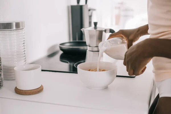 Abgeschnittene Ansicht einer afrikanisch-amerikanischen Frau, die in der Küche Milch in eine Schüssel mit Cornflakes gießt — Stockfoto