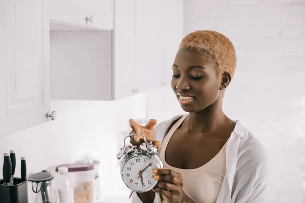 Bela mulher americana africana com cabelo curto segurando relógio em citchen branco — Fotografia de Stock