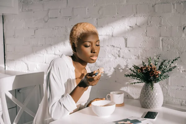 Schöne afrikanisch-amerikanische Frau isst Cornflakes in weißer Küche — Stockfoto