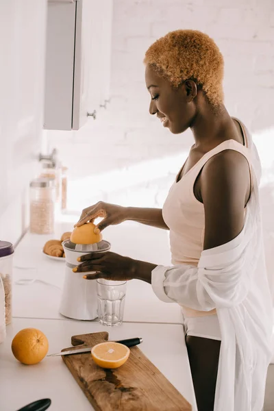 Vista laterale di attraente donna africana americana spremitura arancione — Foto stock