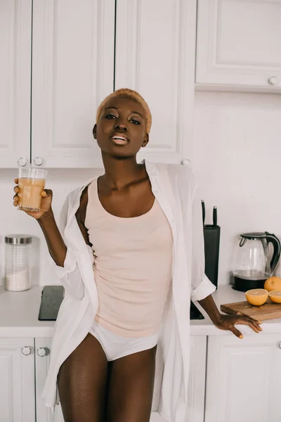 Впевнено афро-американських жінки, що тримає склянку апельсинового соку білий кухні — стокове фото