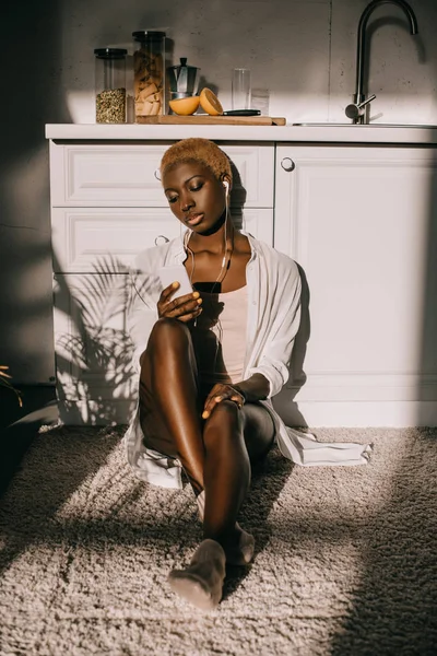 Красивая африканская американка слушает музыку в наушниках на белой кухне — стоковое фото