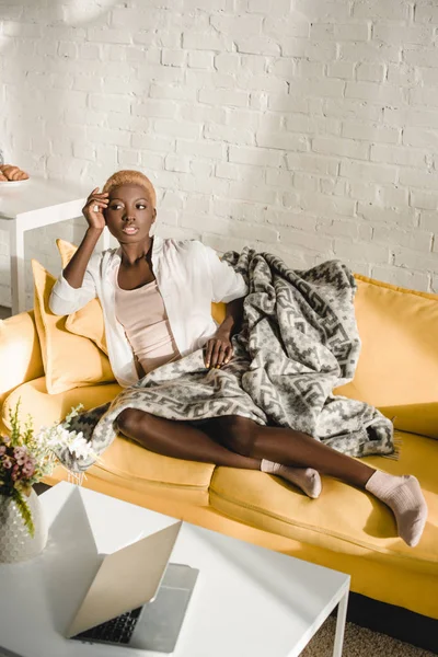 Dreamy african american woman lying on yellow sofa in living room — Stock Photo