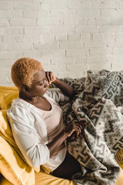 Femme afro-américaine rêveuse couchée sur un canapé jaune sous couverture — Photo de stock