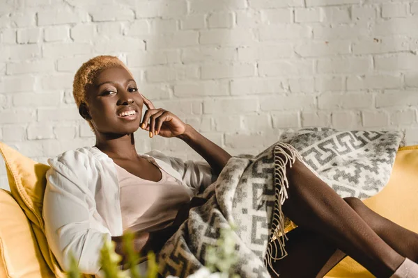 Весёлая африканская американка лежит на жёлтом диване под одеялом — стоковое фото