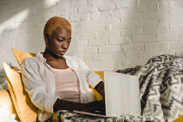 Focalisé afro-américaine femme à l'aide d'un ordinateur portable sur canapé jaune — Photo de stock