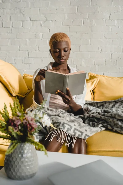 Attrayant afro-américaine livre de lecture femme sur canapé jaune — Photo de stock