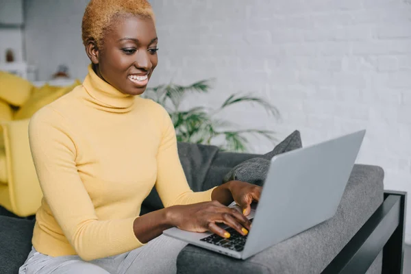 Femme afro-américaine gaie utilisant un ordinateur portable dans le salon — Photo de stock