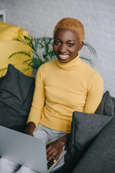 Cheerful african american woman using laptop on sofa — Stock Photo