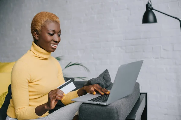 Atractiva mujer afroamericana utilizando el ordenador portátil y la celebración de la tarjeta de crédito - foto de stock