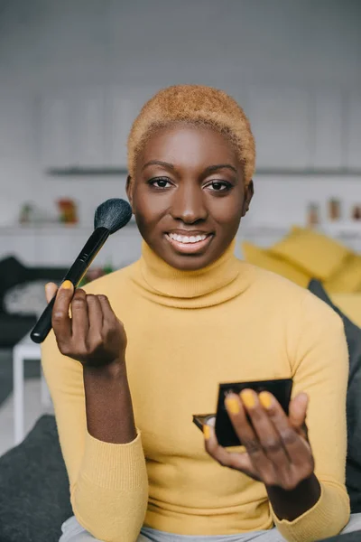 Mujer americana africana alegre aplicando polvo con cepillo cosmético - foto de stock