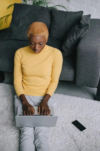 Afro-américaine femme assise sur le tapis et en utilisant un ordinateur portable — Photo de stock