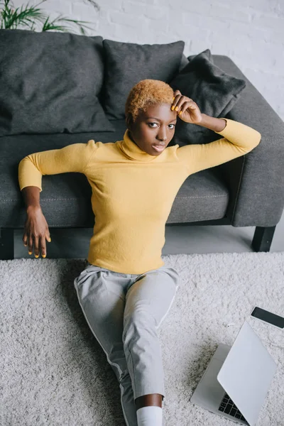 Atractiva mujer afroamericana sentada en la alfombra en la sala de estar - foto de stock