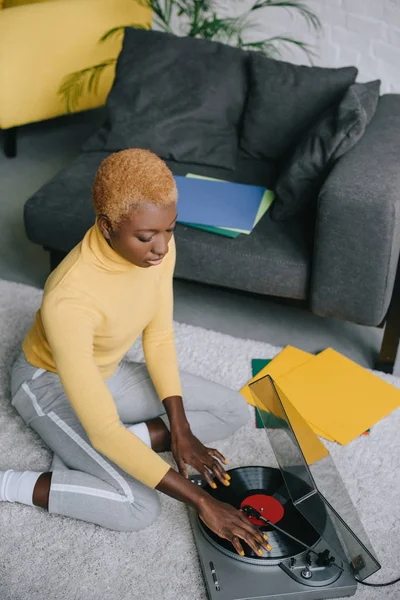 Attractive african american woman using record player on carpet — Stock Photo