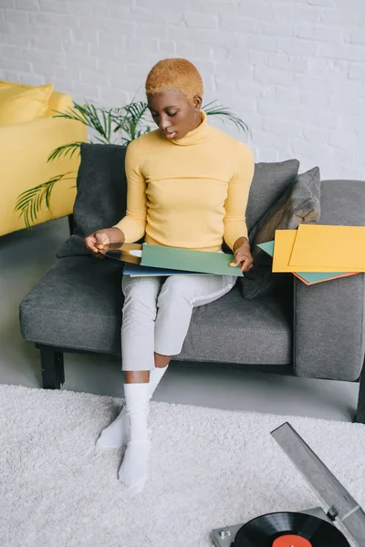 Pensive african american woman sitting with vinyl records in living room — Stock Photo