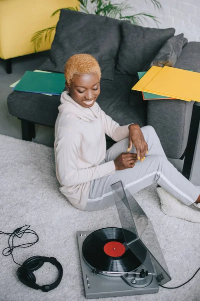 African american woman smiling and sitting on carpet near record player — Stock Photo