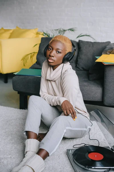 African american woman sitting on carpet and listening music in headphones — Stock Photo