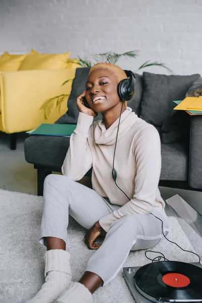 Beautiful african american woman sitting on carpet and listening music in headphones — Stock Photo