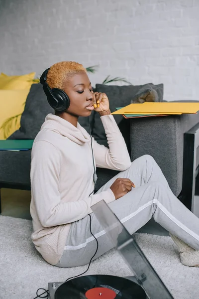 African american woman sitting on carpet and listening music in headphones — Stock Photo