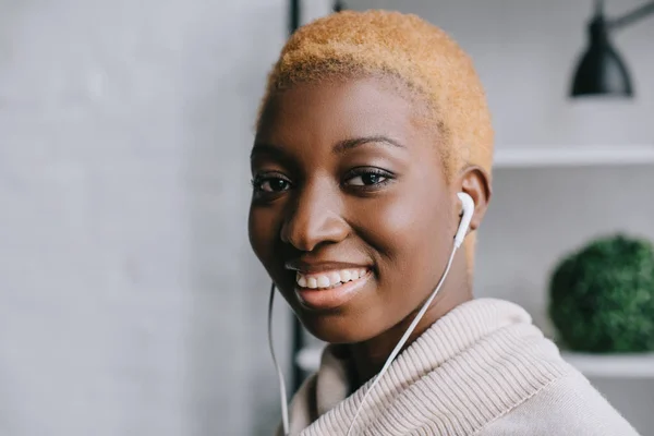 Primer plano de la sonriente mujer afroamericana escuchando música en auriculares - foto de stock
