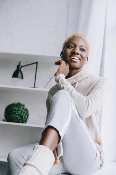 Femme afro-américaine souriante aux cheveux courts écoutant de la musique dans les écouteurs — Photo de stock